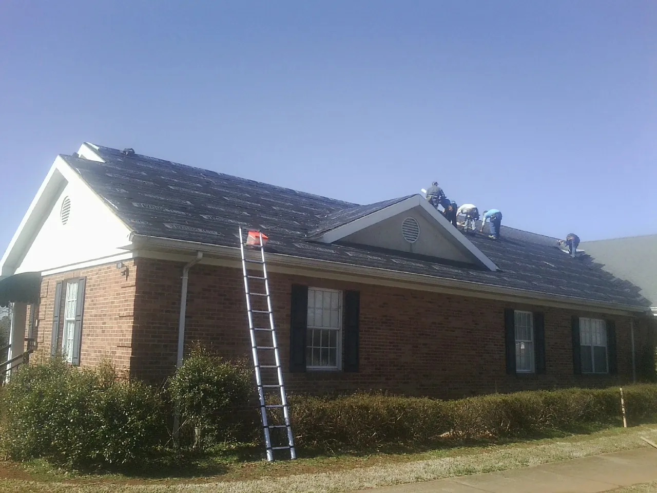 Crew tearing shingles off a brick ranch roof with a ladder set — Emergency Roof Repair work by our crew in Brinklow