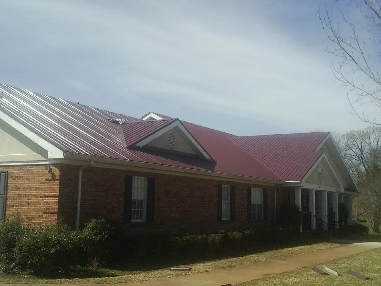 Red metal roof with gabled entries on a long brick building, from a Hail Damage Roof Repair job in Brinklow