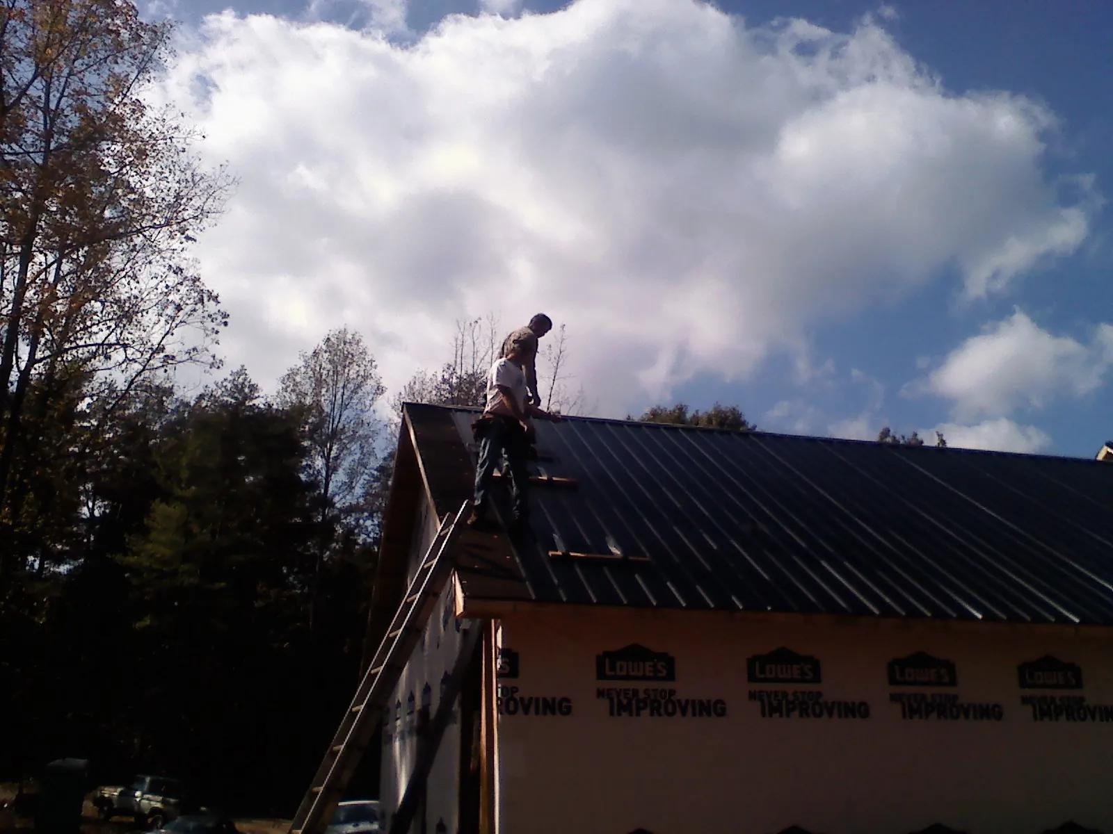 Roofer fastening dark metal panels high against a cloudy sky, from a Roof Inspection job in Brinklow