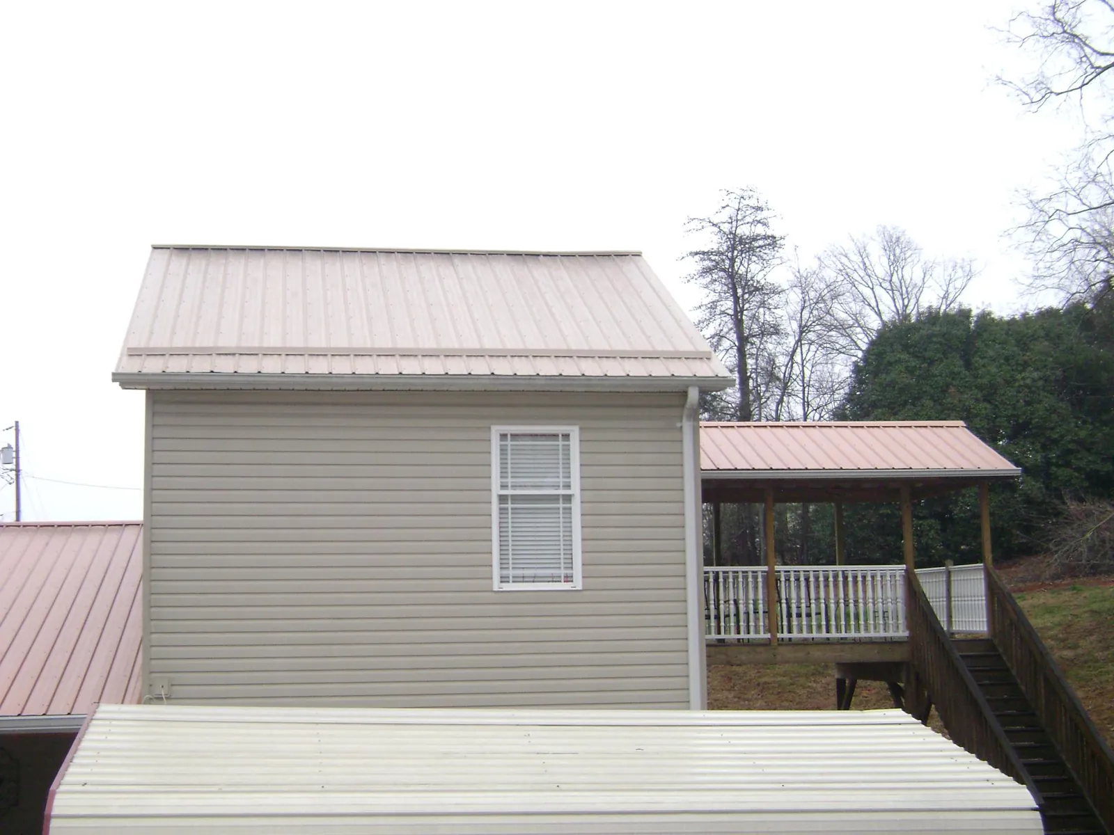 Tan metal roofs on a two story addition and attached porch, from a Roof Replacement job in Brinklow